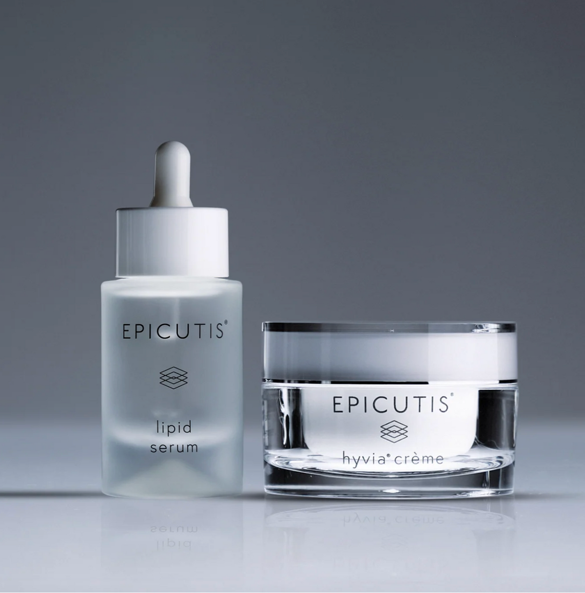 Epicutis skincare set featuring a clear glass dropper bottle of Lipid Serum and a matching clear glass jar of Hyalucreme, set against a dark gray gradient studio background.